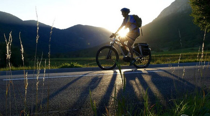 Cycliste roulant devant soleil et montagne.